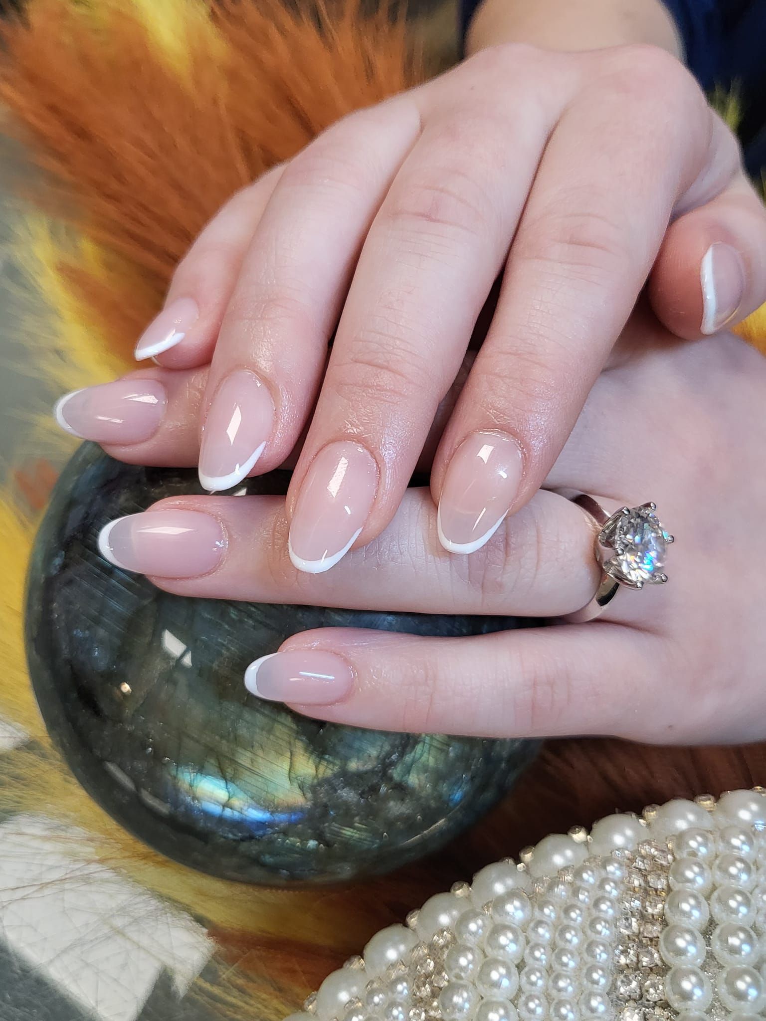 Manicured nails with white French tips, a hand wearing a ring, resting on a decorative stone.