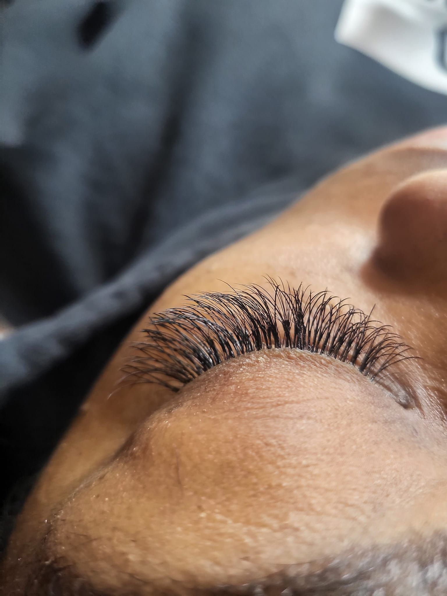 Close-up of a person's closed eye with long, dark eyelashes. Light skin is visible.