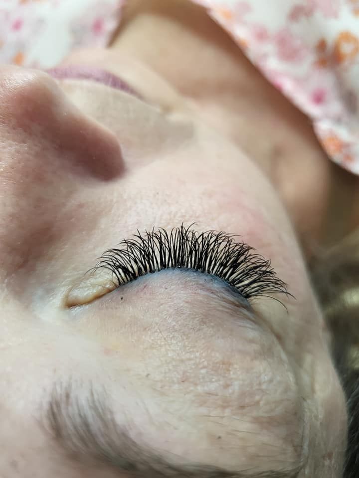 Close-up of a person's closed eye, showcasing dark, full eyelash extensions against pale skin.