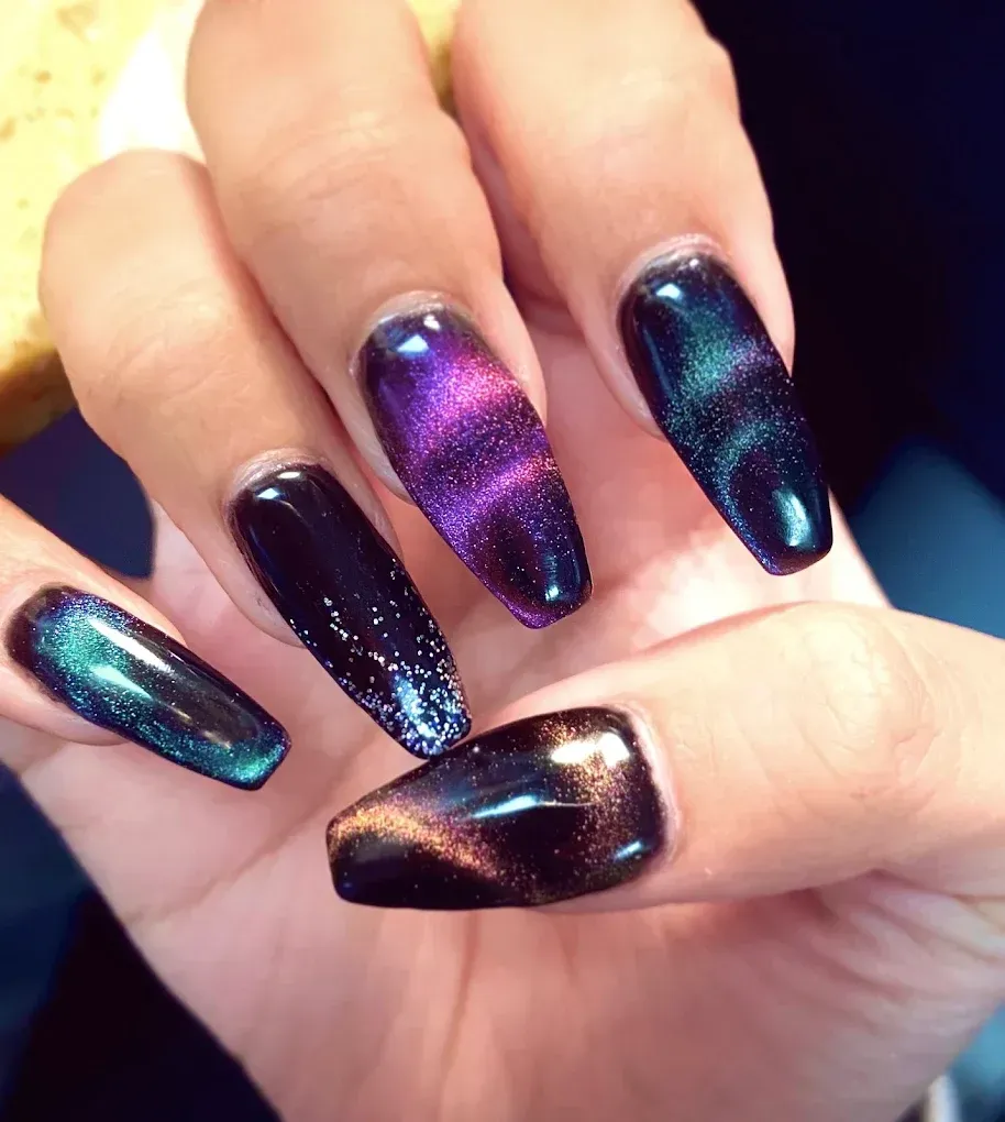 Close-up of a hand with long, coffin-shaped nails painted with a galaxy-themed cat-eye effect in shades of purple, blue, and green.