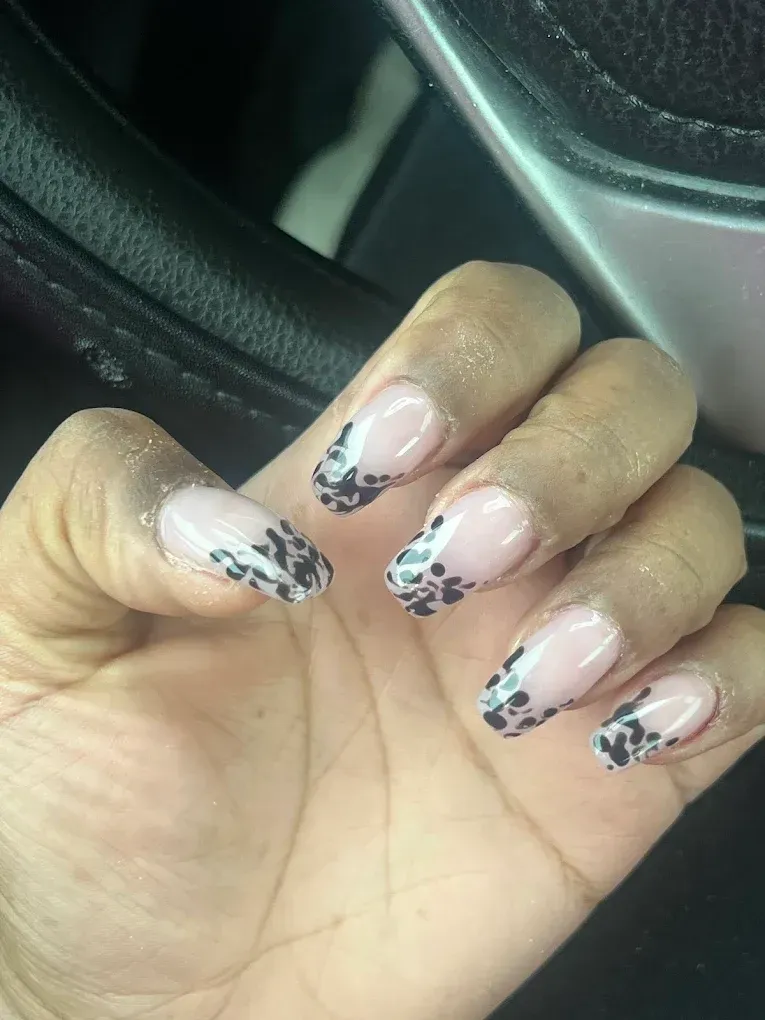 Hand with almond-shaped nails featuring French tips with black floral pattern.
