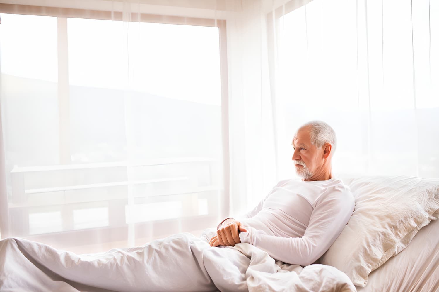 An Elderly Man is Laying in an Adjustable Bed Looking Out the Window — Bryants Beds and Mattresses In Lismore, NSW