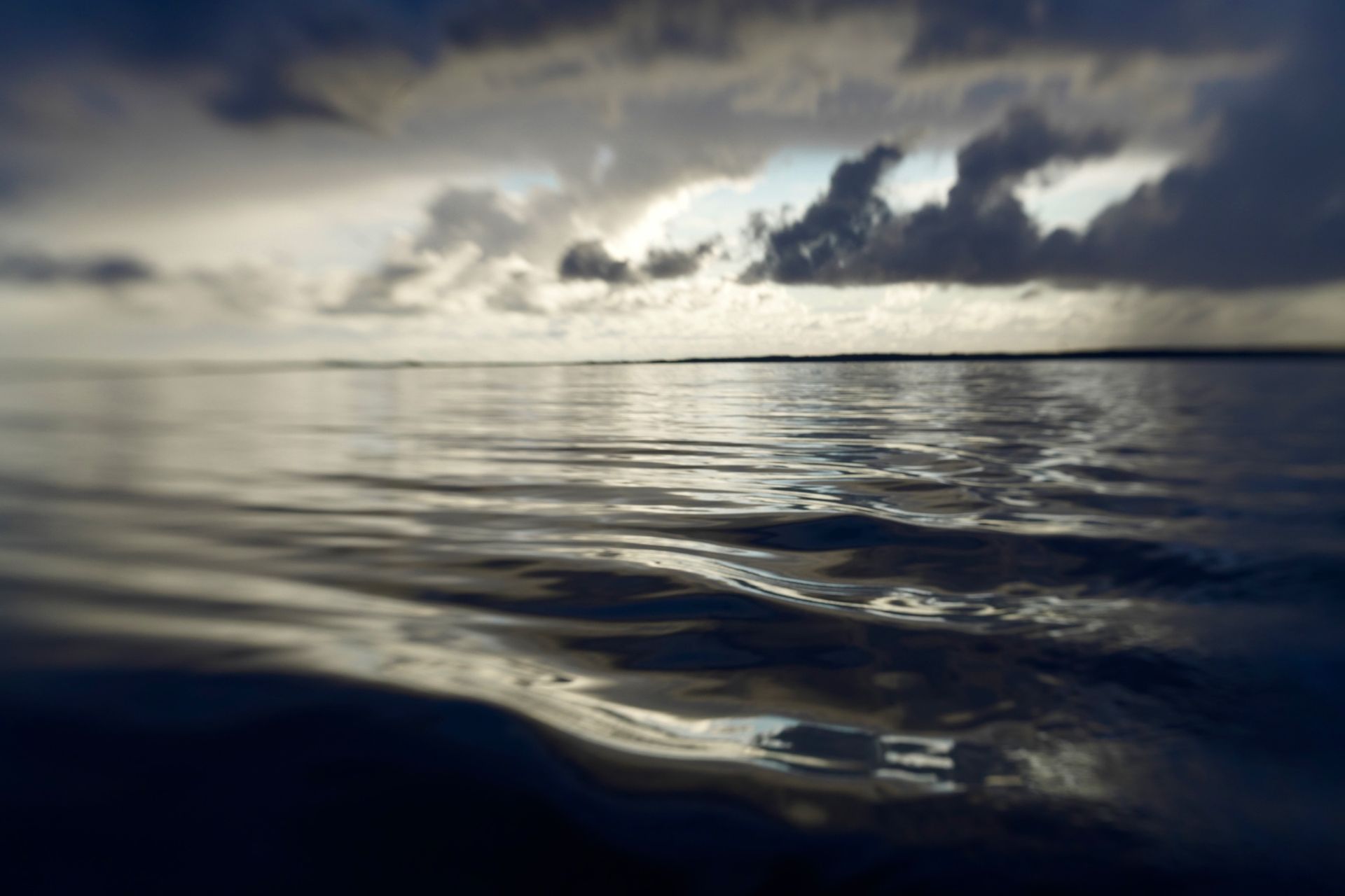 Calm ocean water reflects a cloudy, stormy sky.