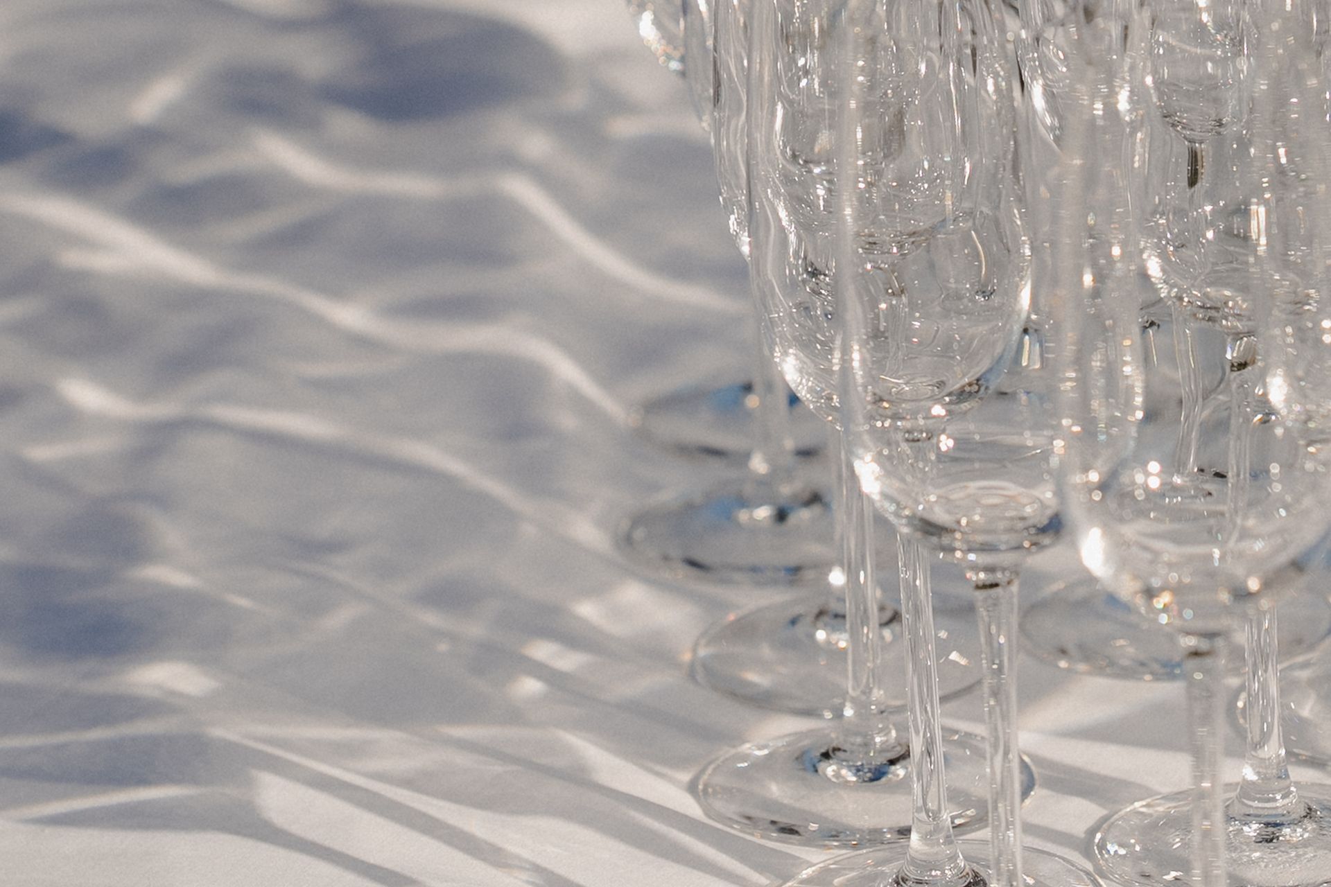Rows of champagne flutes casting patterned shadows on a white surface.