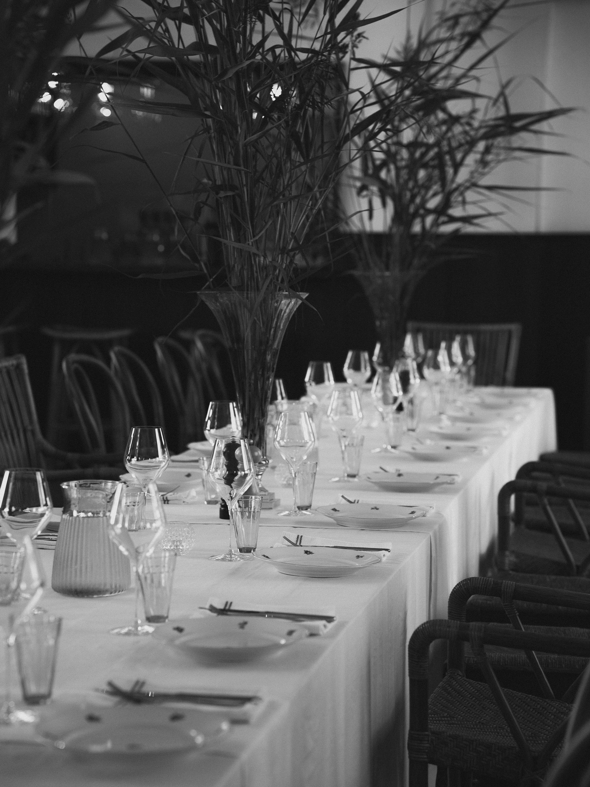 Formal dining table set for a meal, with glasses, plates, and tall floral centerpieces.