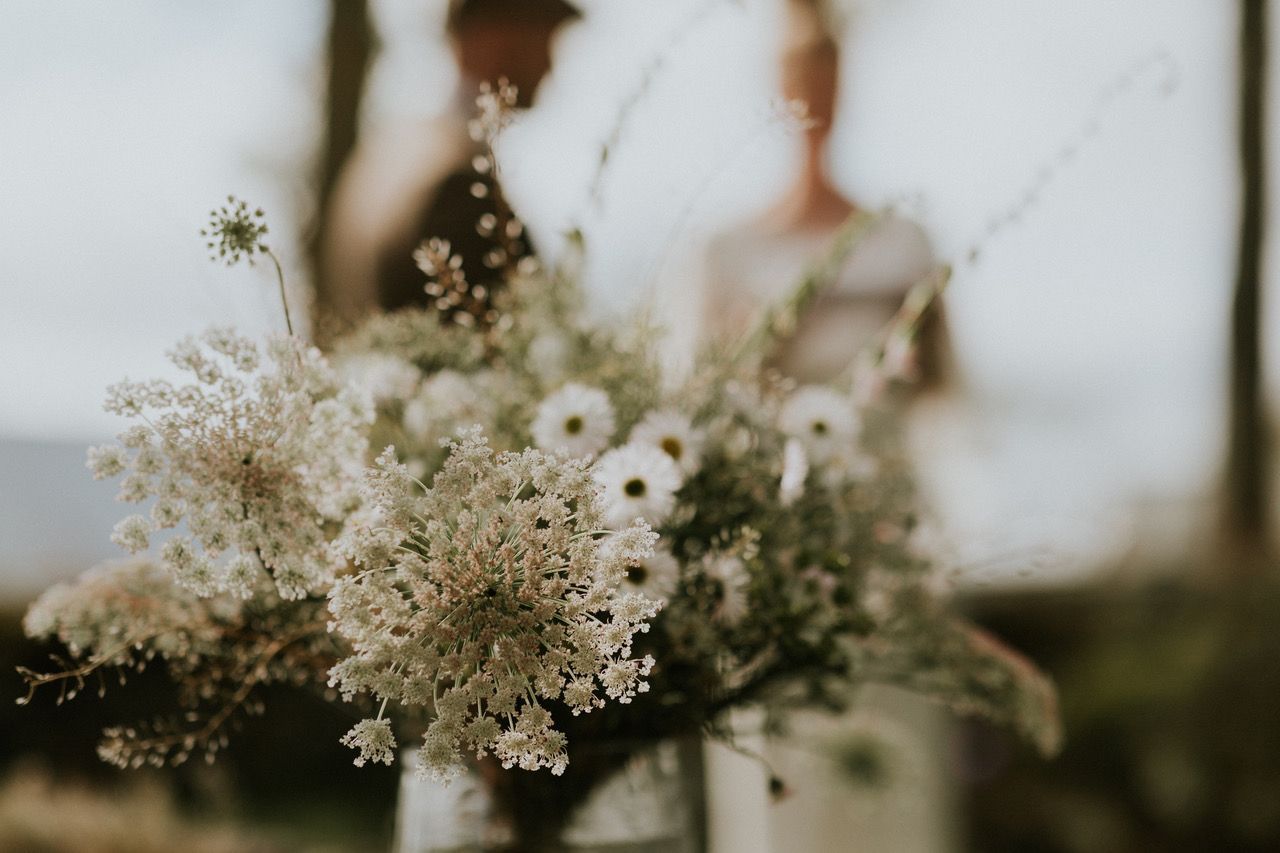 Bouquet of white flowers, in focus; couple blurred in background.