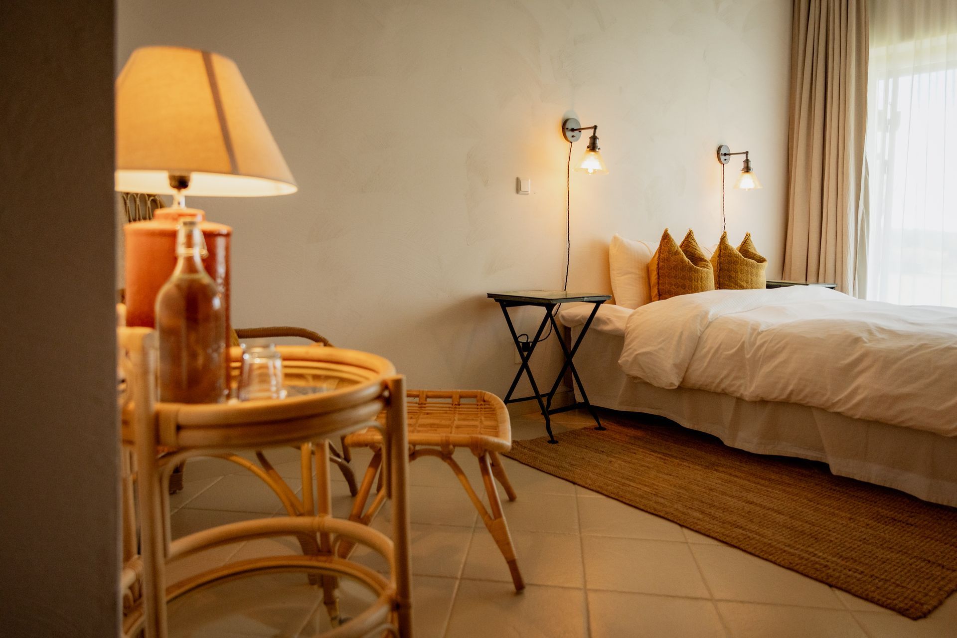 Cozy bedroom with rattan furniture, bed, and decorative lamps. Neutral tones create a relaxing atmosphere.