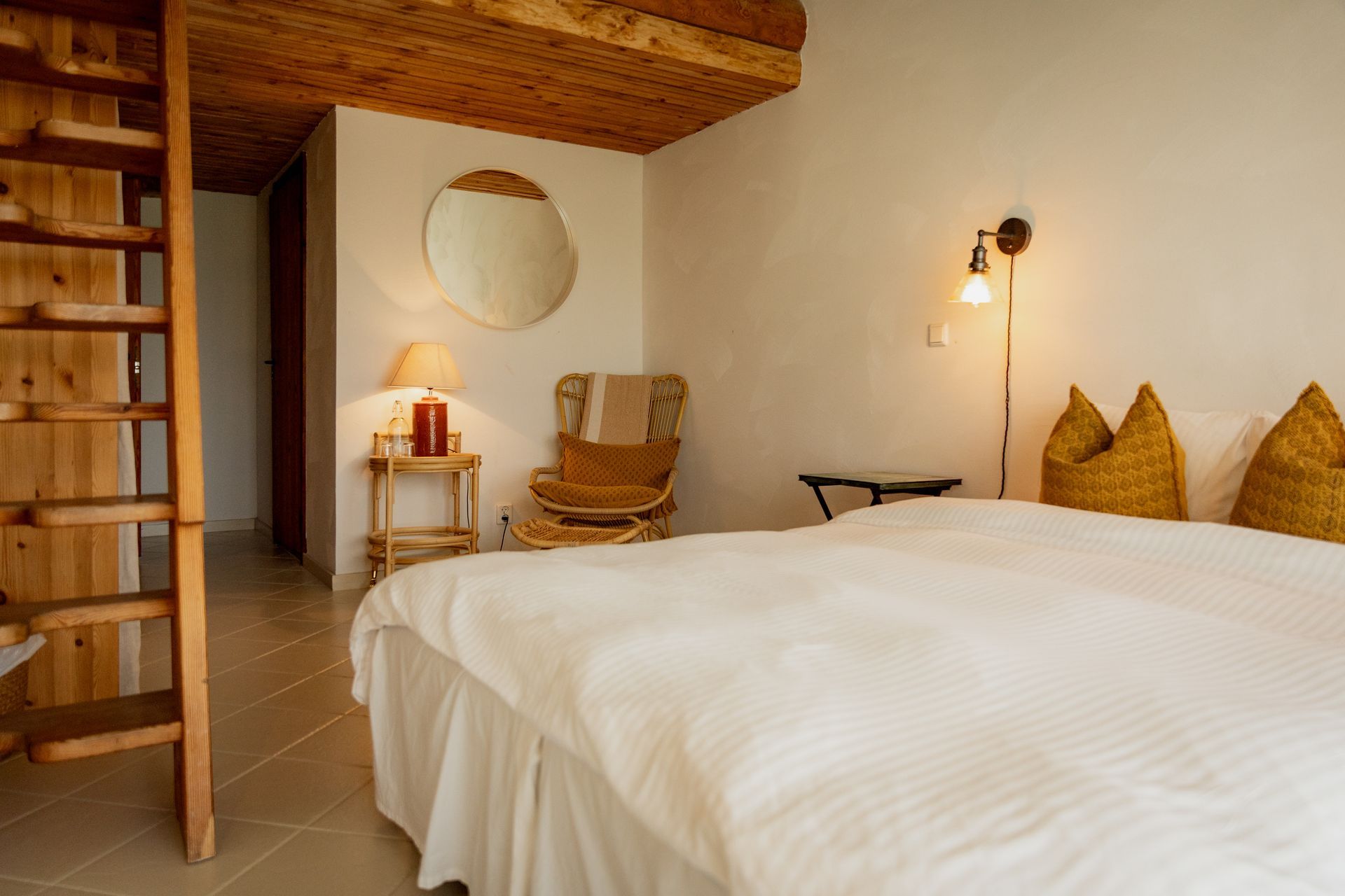 Bedroom with bed, wicker chair, wooden ceiling, and staircase.