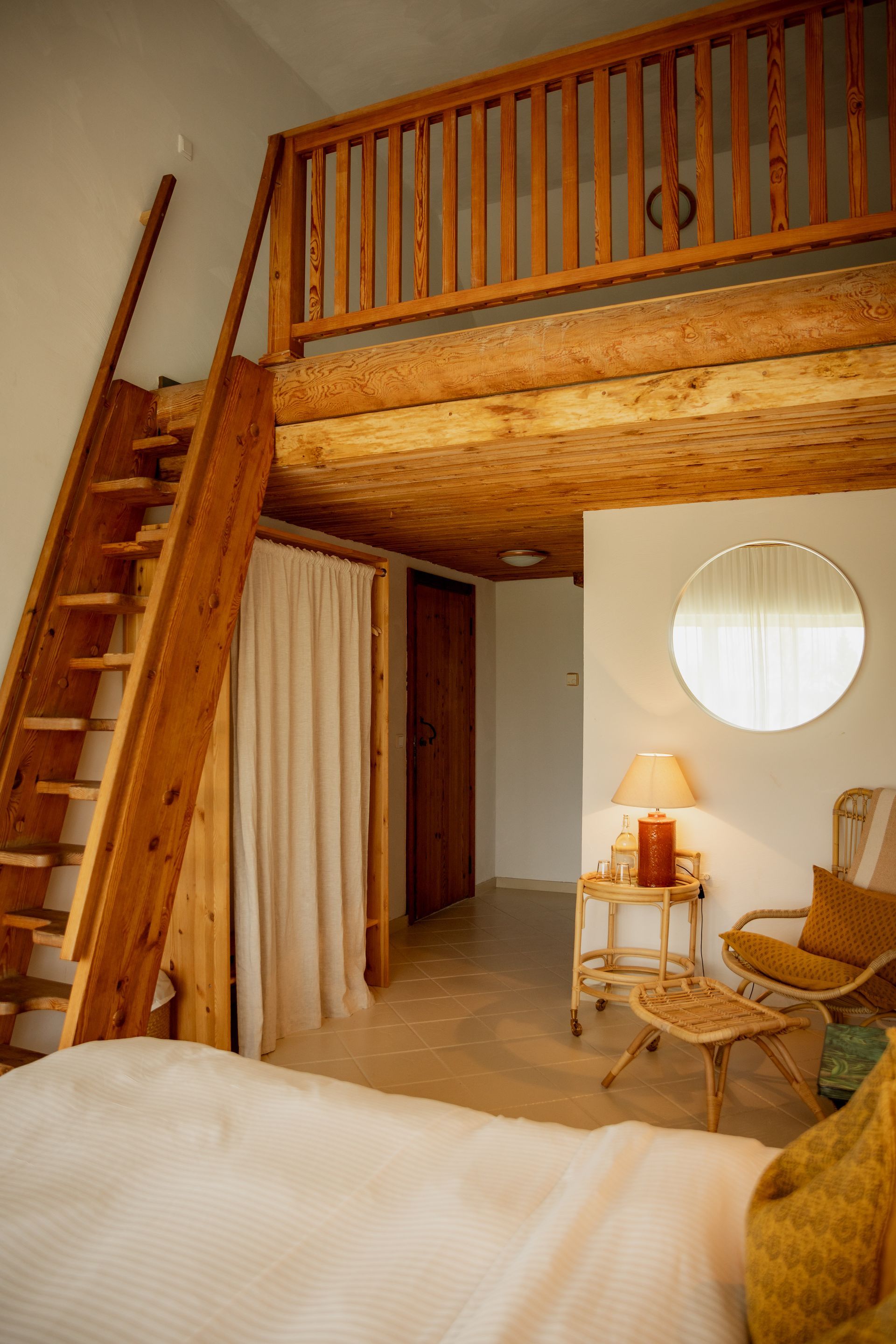 Bedroom with wooden loft, ladder, and a round mirror. Includes chair, lamp, and neutral colors.