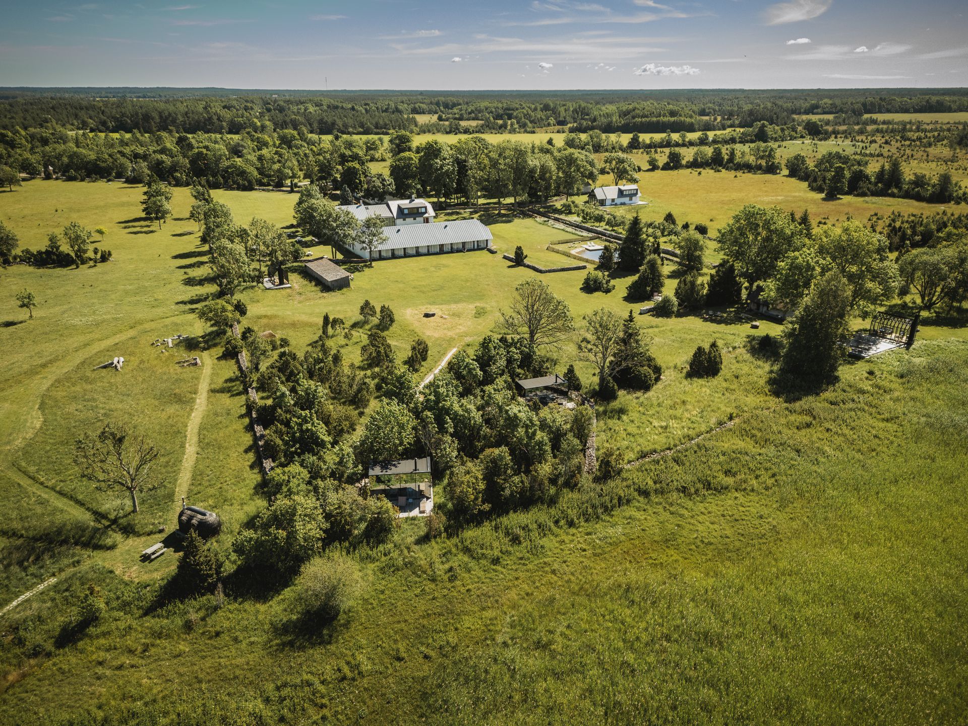 Aerial view of a green field with buildings and trees under a blue sky on a sunny day.
