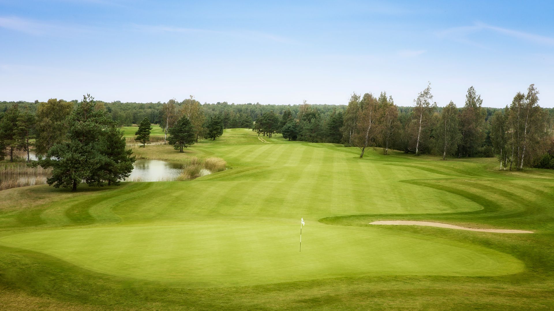Golf course with green grass, trees, water, and blue sky.
