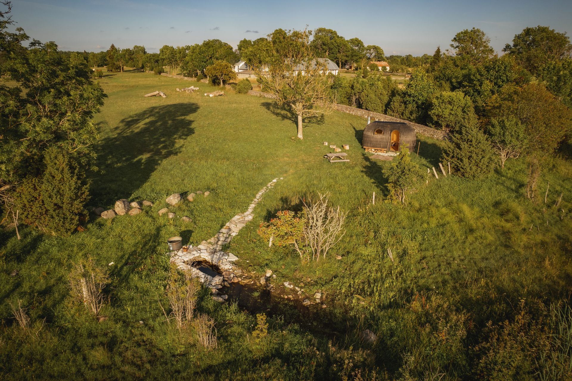 Green field with stone structures, trees, and a small building in the distance.
