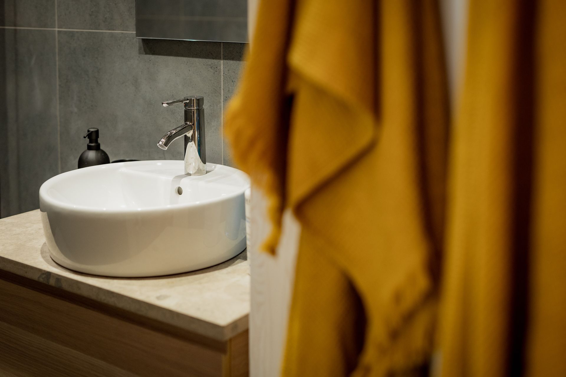 White sink and faucet on a stone counter, with yellow towels hanging in the foreground.