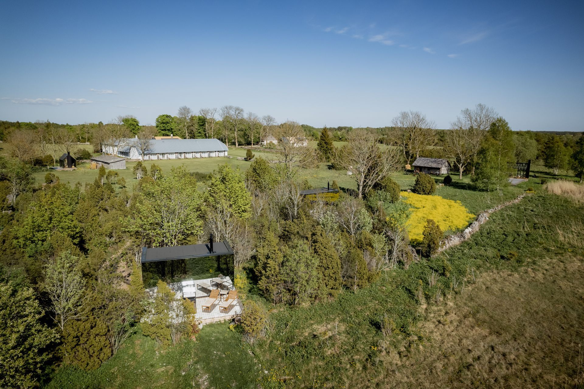 Aerial view of several buildings surrounded by trees and a field under a blue sky.