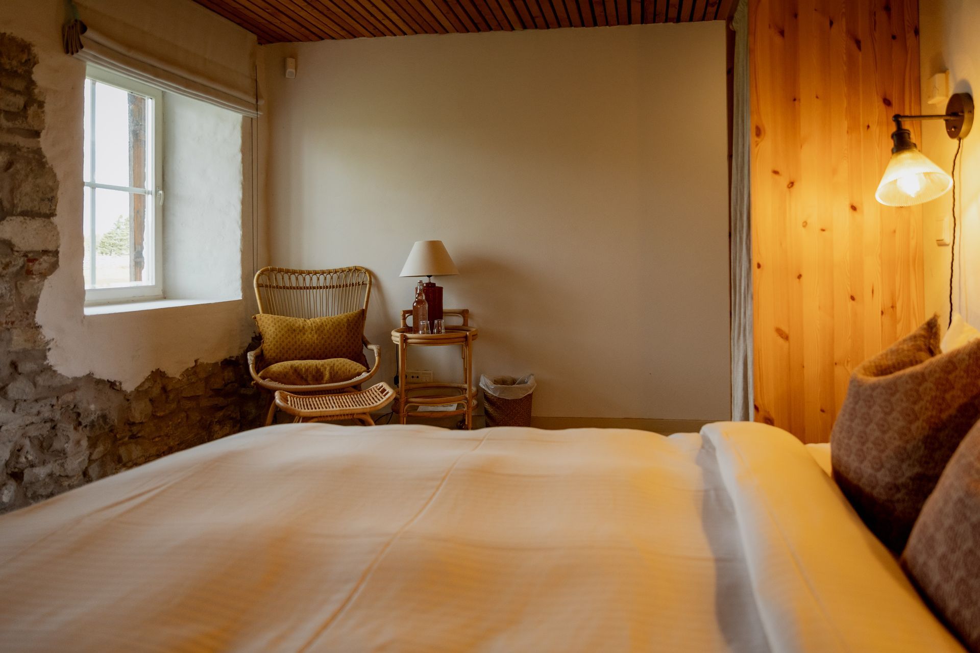 Cozy bedroom with bed, wicker chair, small table, and warm wood accents.