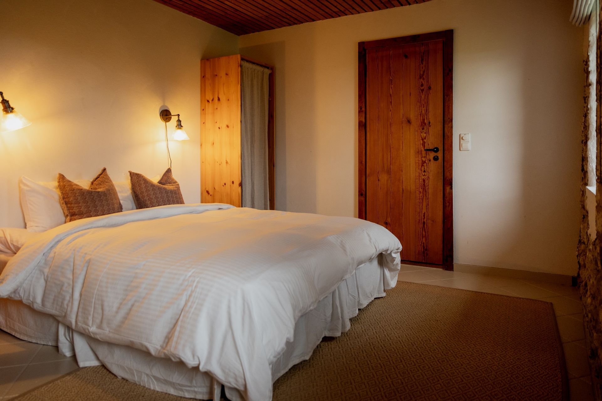 Bedroom with white bedding, brown pillows, wooden door and closet, and rug.