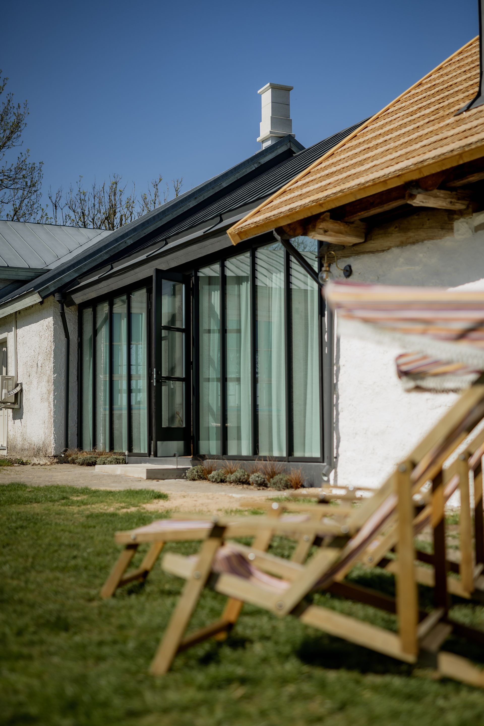 Exterior of a white house with a modern glass extension and wooden folding chairs on the lawn.
