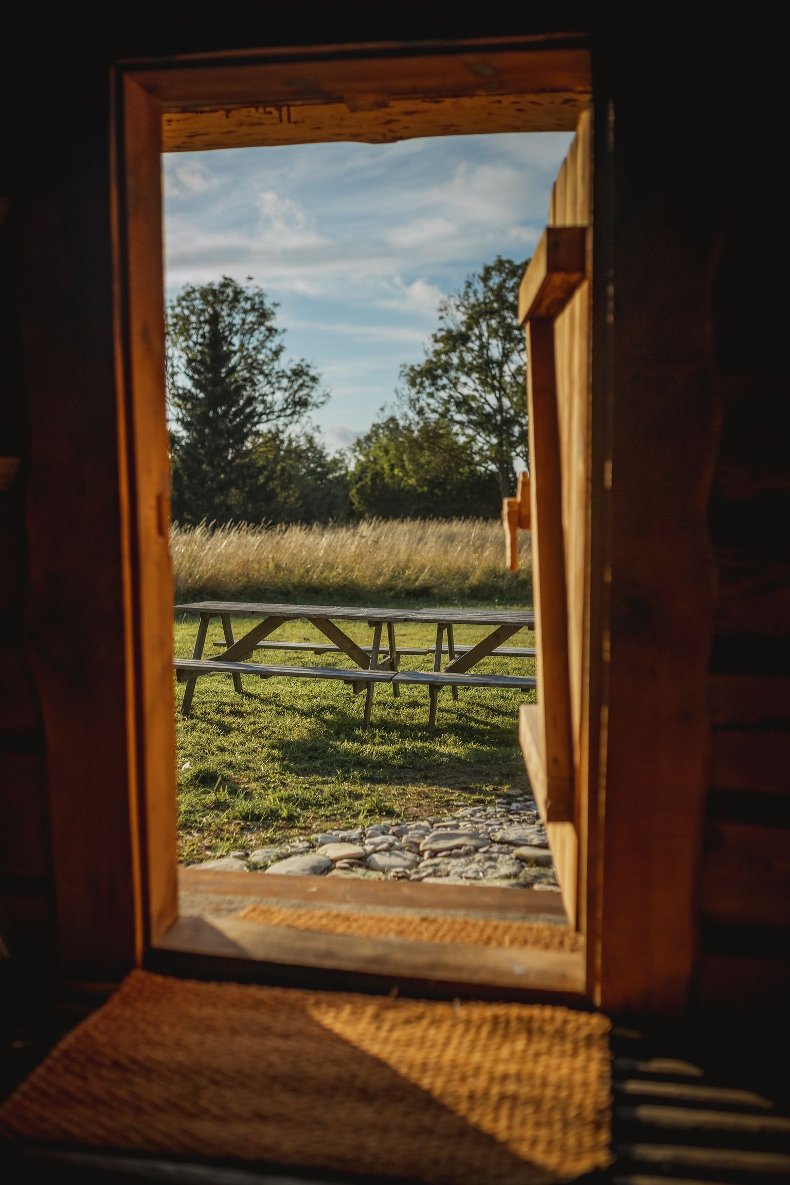 Wooden door frame opens to a field with a picnic table and trees under a blue sky.
