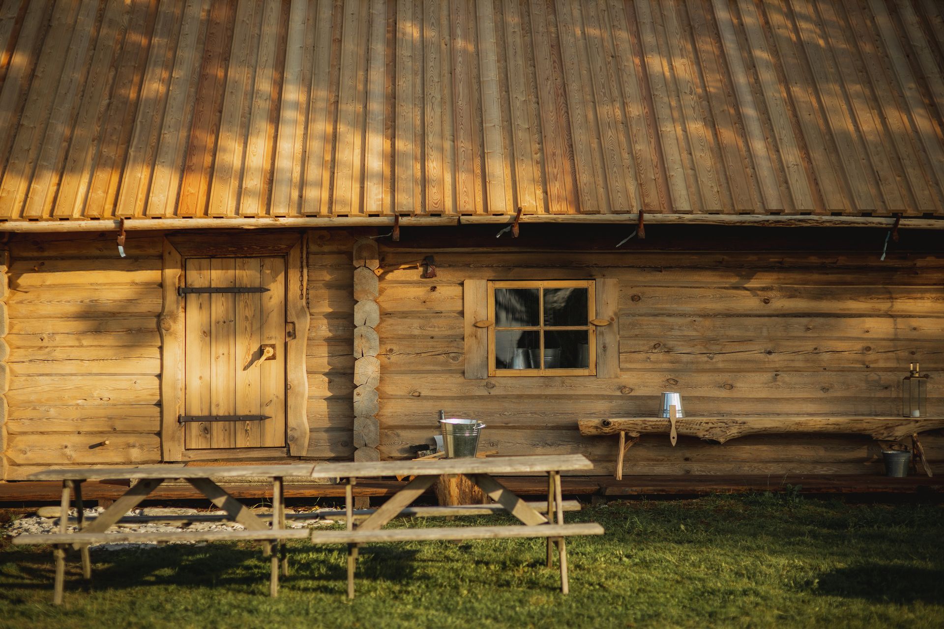 Wooden cabin with a picnic table on a grassy lawn. Sunlight bathes the exterior.