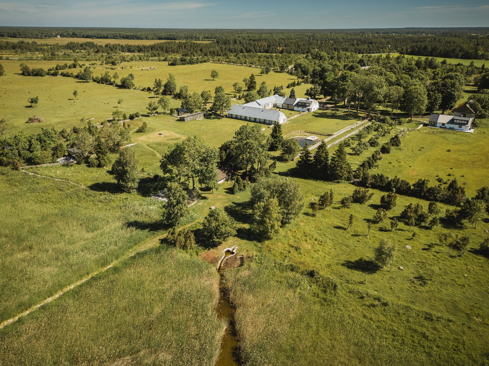 Green fields and trees surrounding a cluster of white buildings under a blue sky.