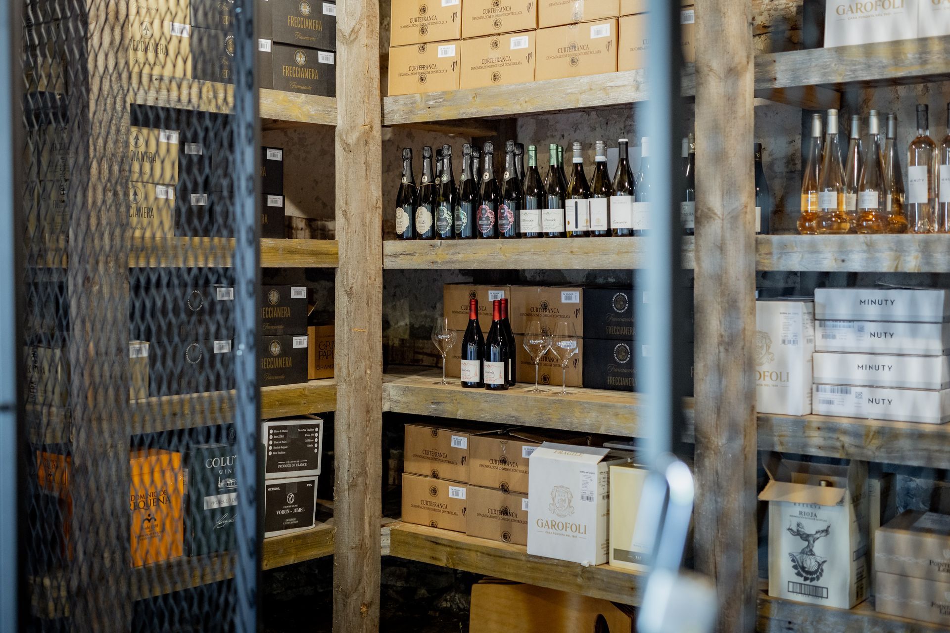 Wine bottles and boxes on wooden shelves in a cellar.