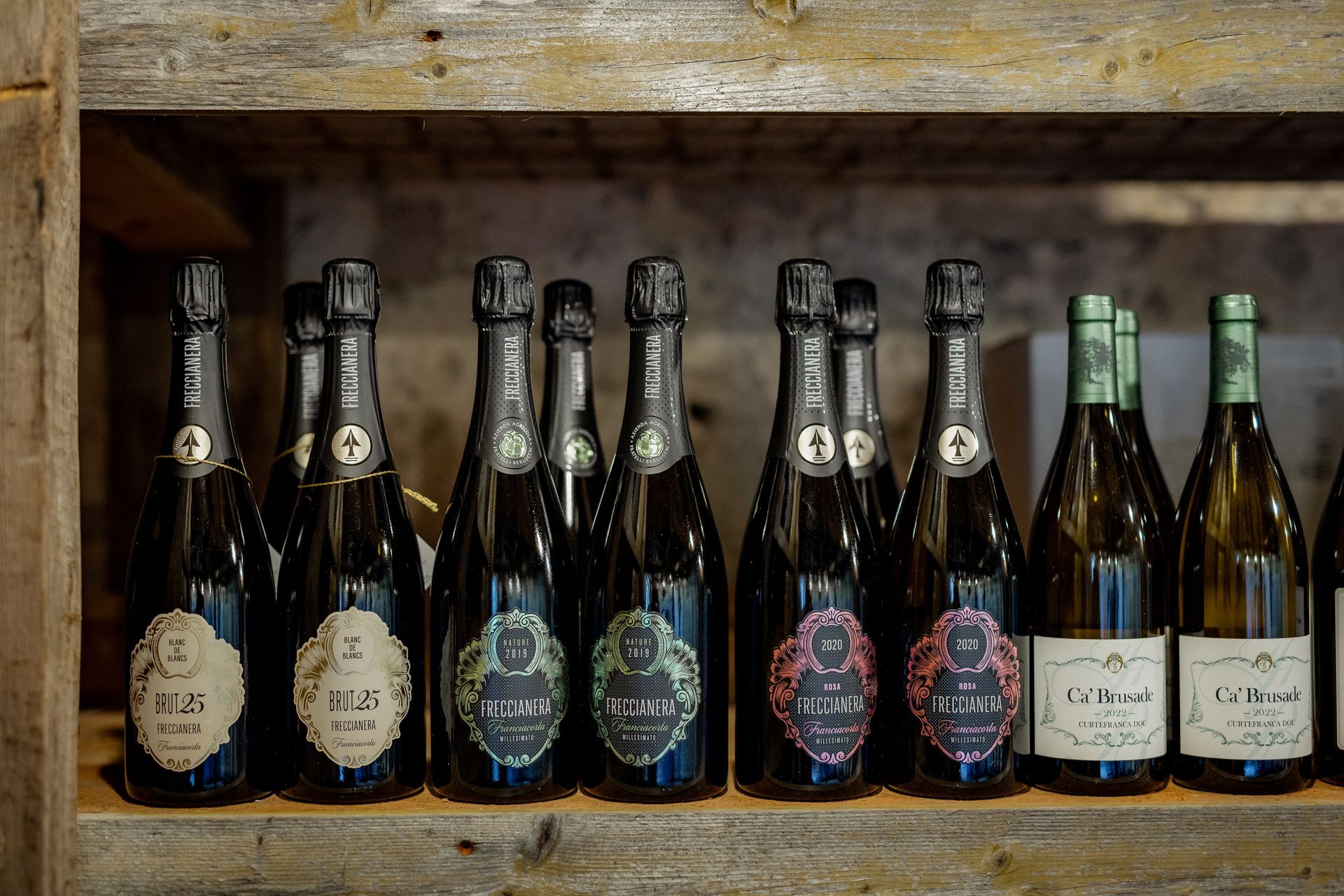 Wine bottles on wooden shelf, various labels, dark glass.