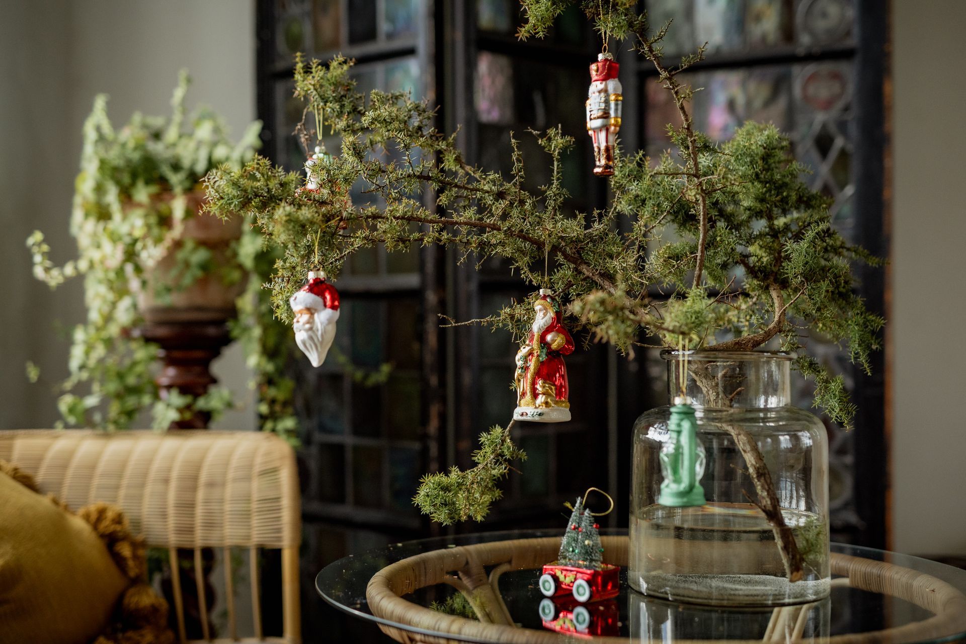 A Christmas tree with ornaments in a clear glass vase, set in front of a dark cabinet.