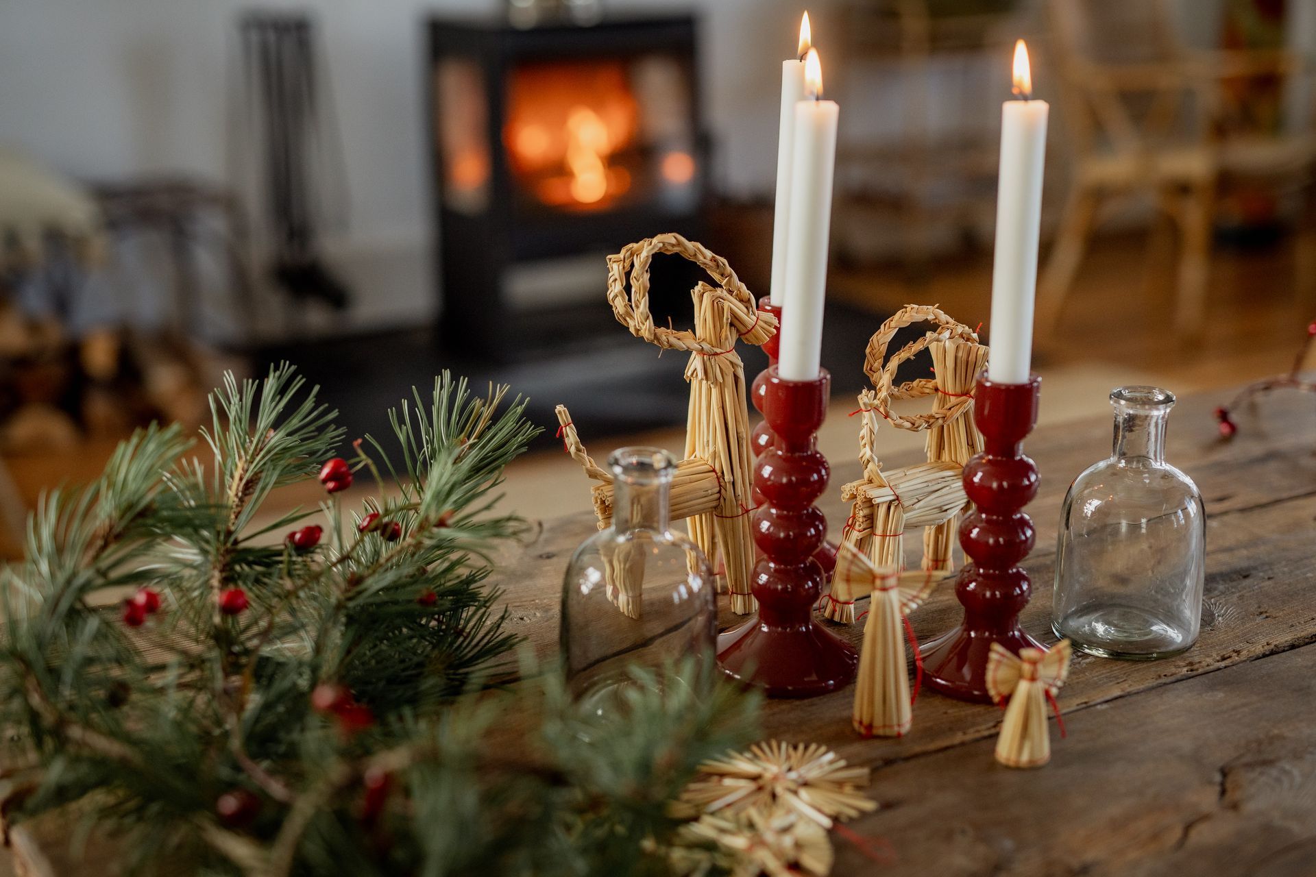 Festive holiday table setting with lit candles, greenery, and a fireplace in the background.