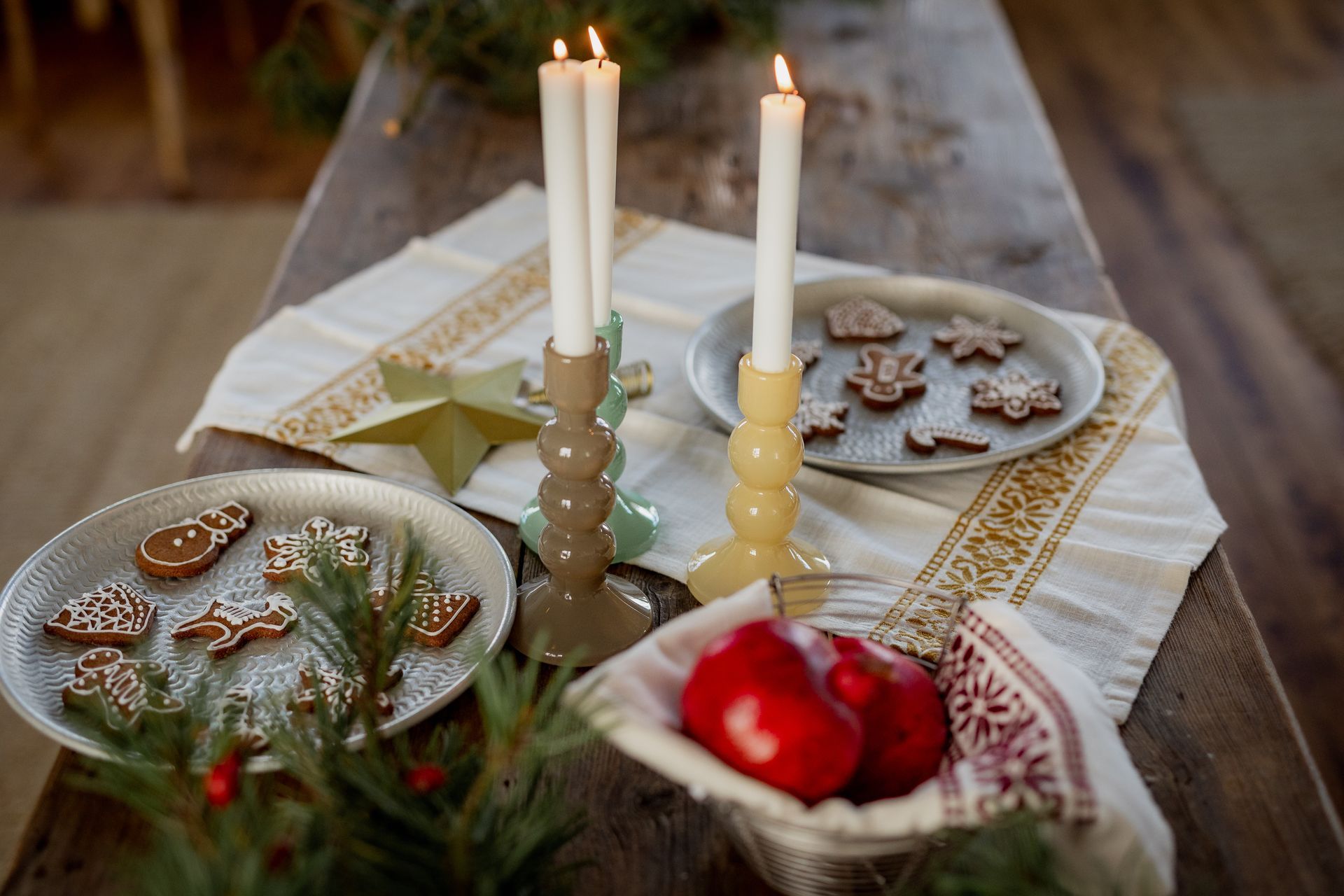 Table setting with lit candles, gingerbread cookies on plates, and red apples in a basket.