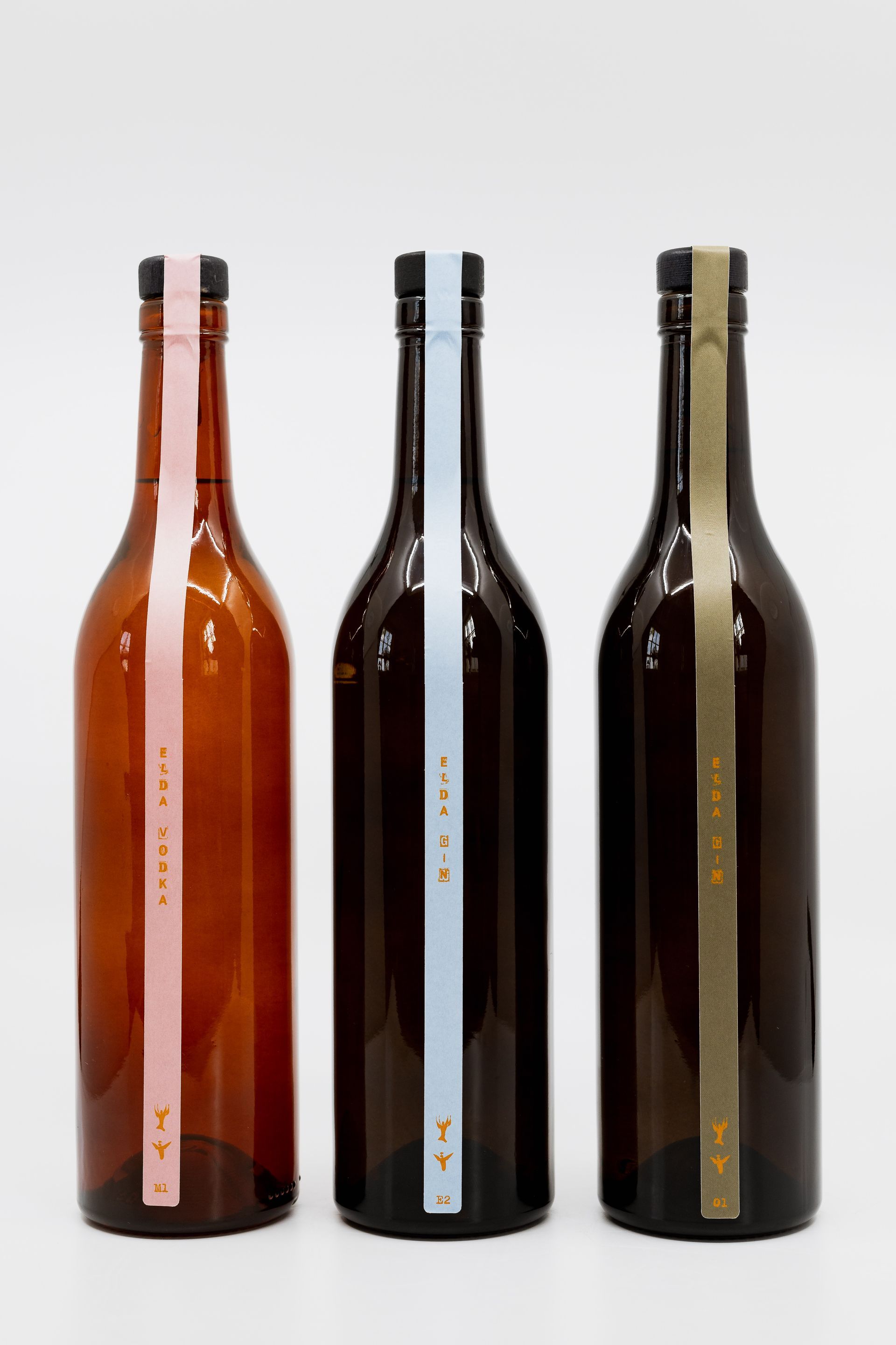 Three brown liquor bottles with colored labels: pink, light blue, and green.