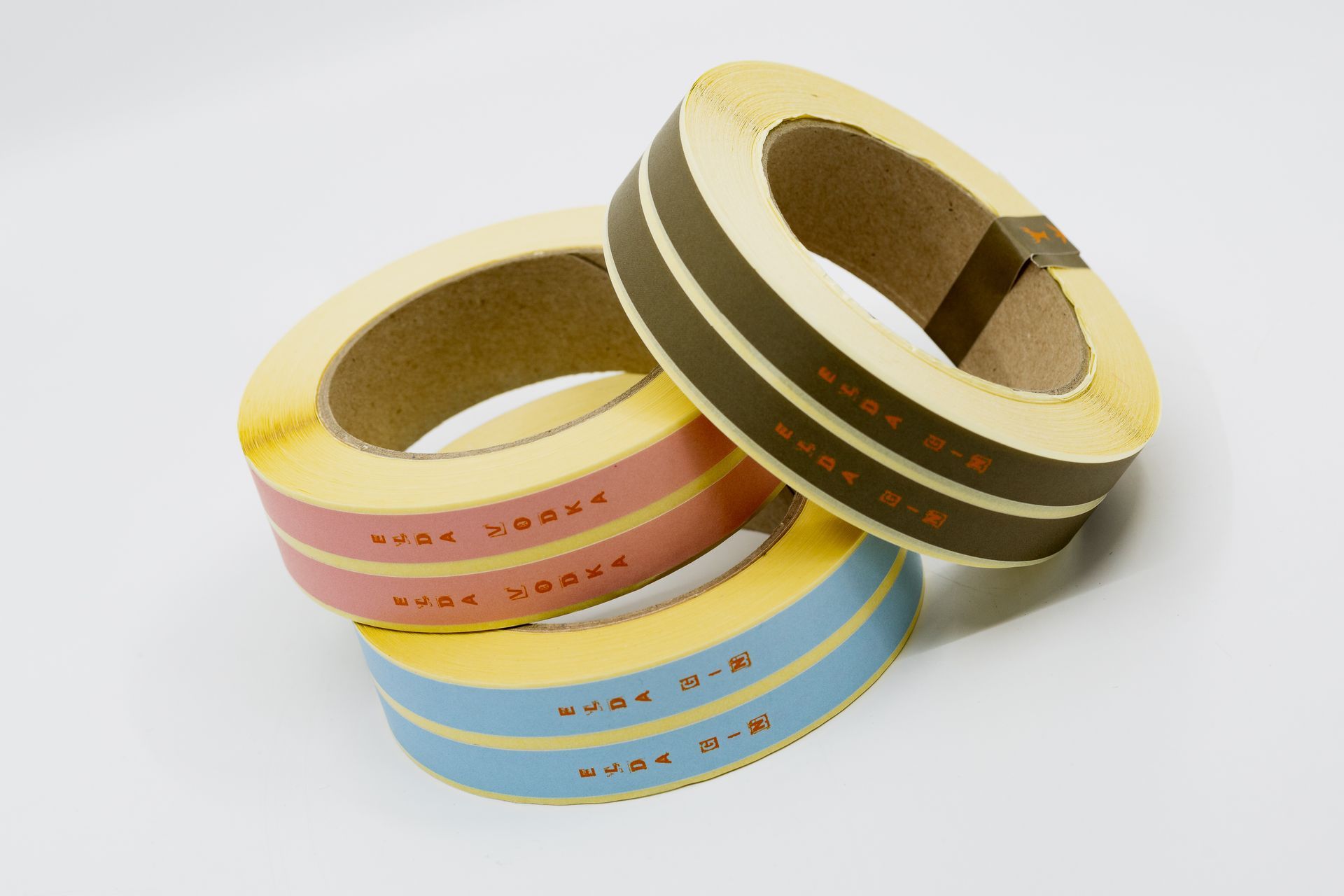 Three rolls of colorful striped tape, pink, brown, and blue, stacked on a white surface.