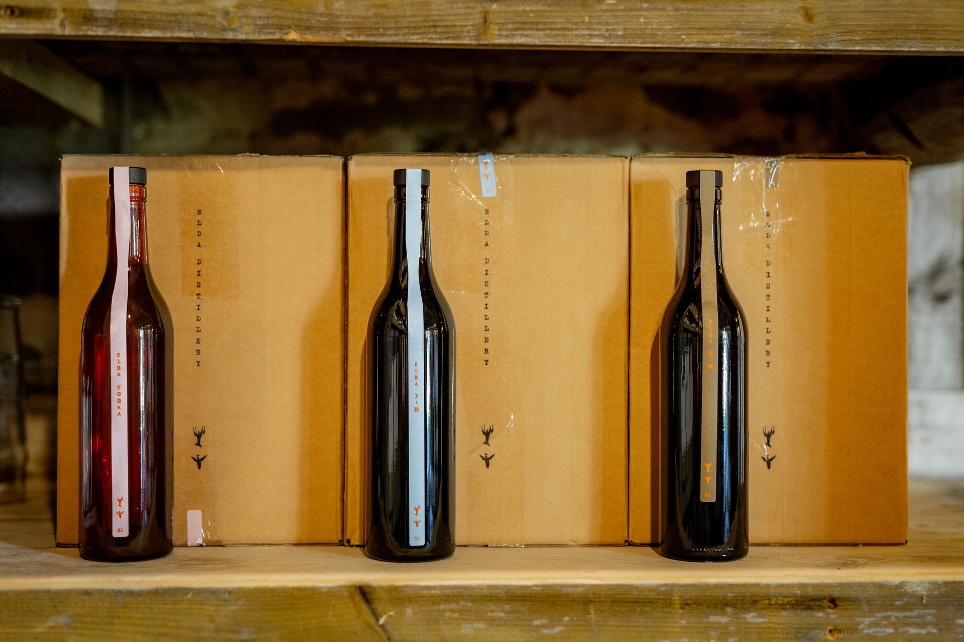 Three wine bottles stand before cardboard boxes on a wooden shelf.