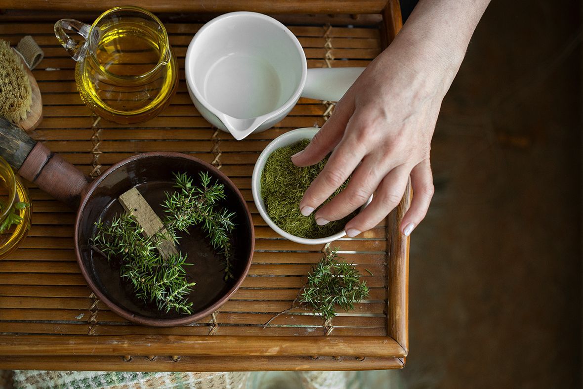 Hand reaching for green herbs on a wooden tray with oil, a white bowl, and sprigs of thyme.