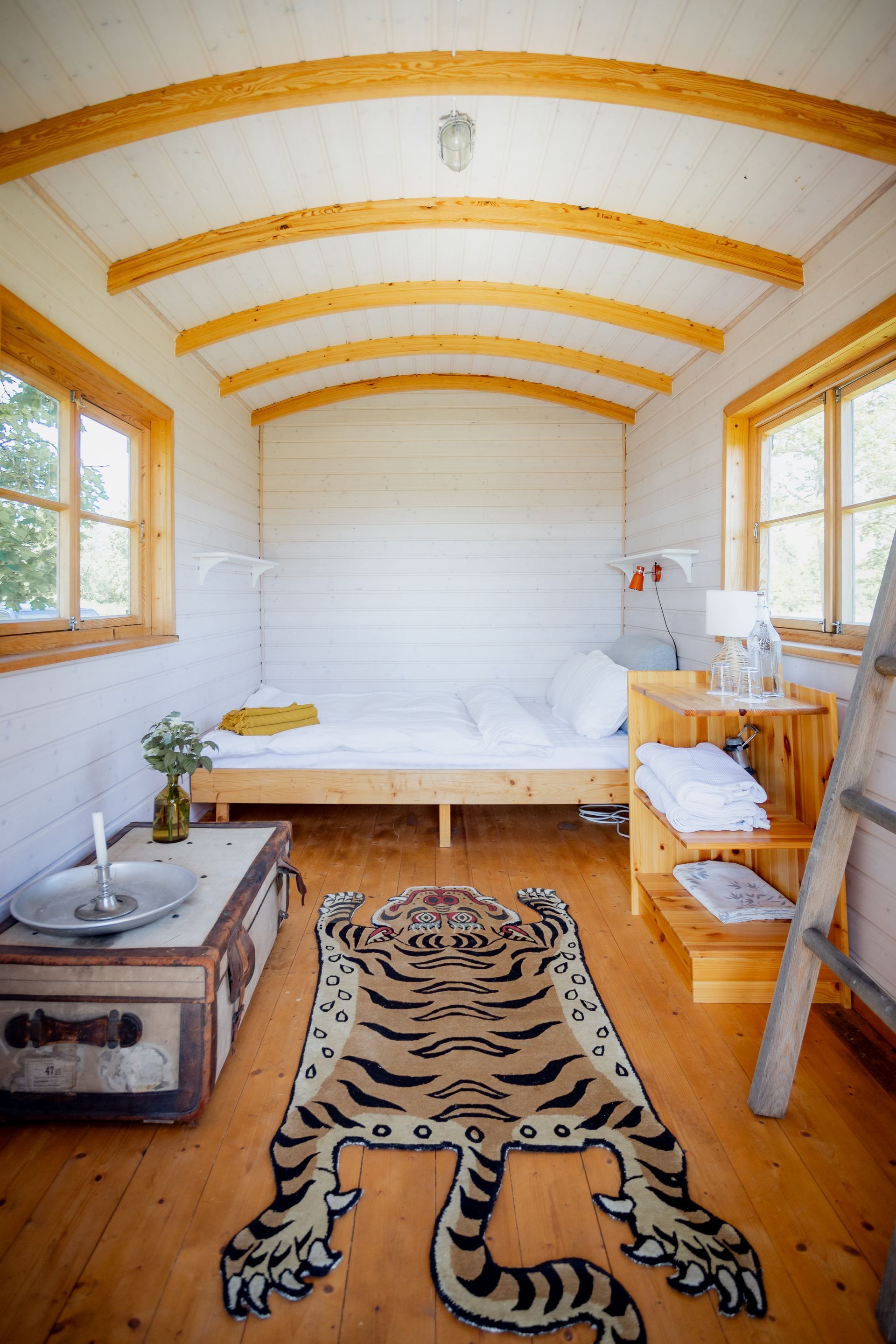 Cozy bedroom inside a wooden wagon with a tiger rug, bed, sink, and small windows.