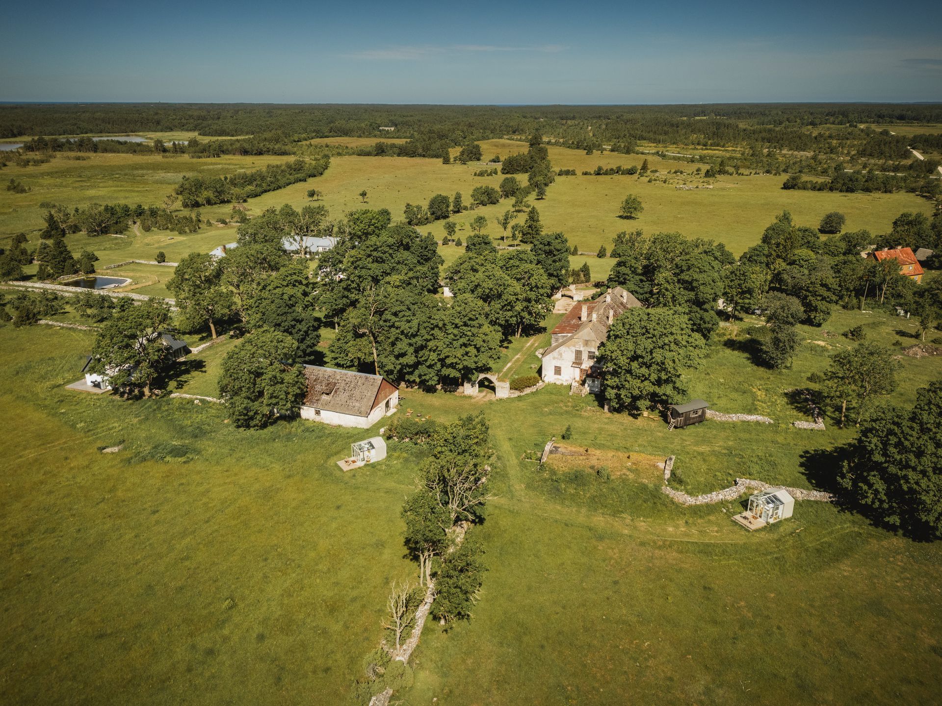 Aerial view of a historic estate with buildings surrounded by green fields and trees under a clear sky.