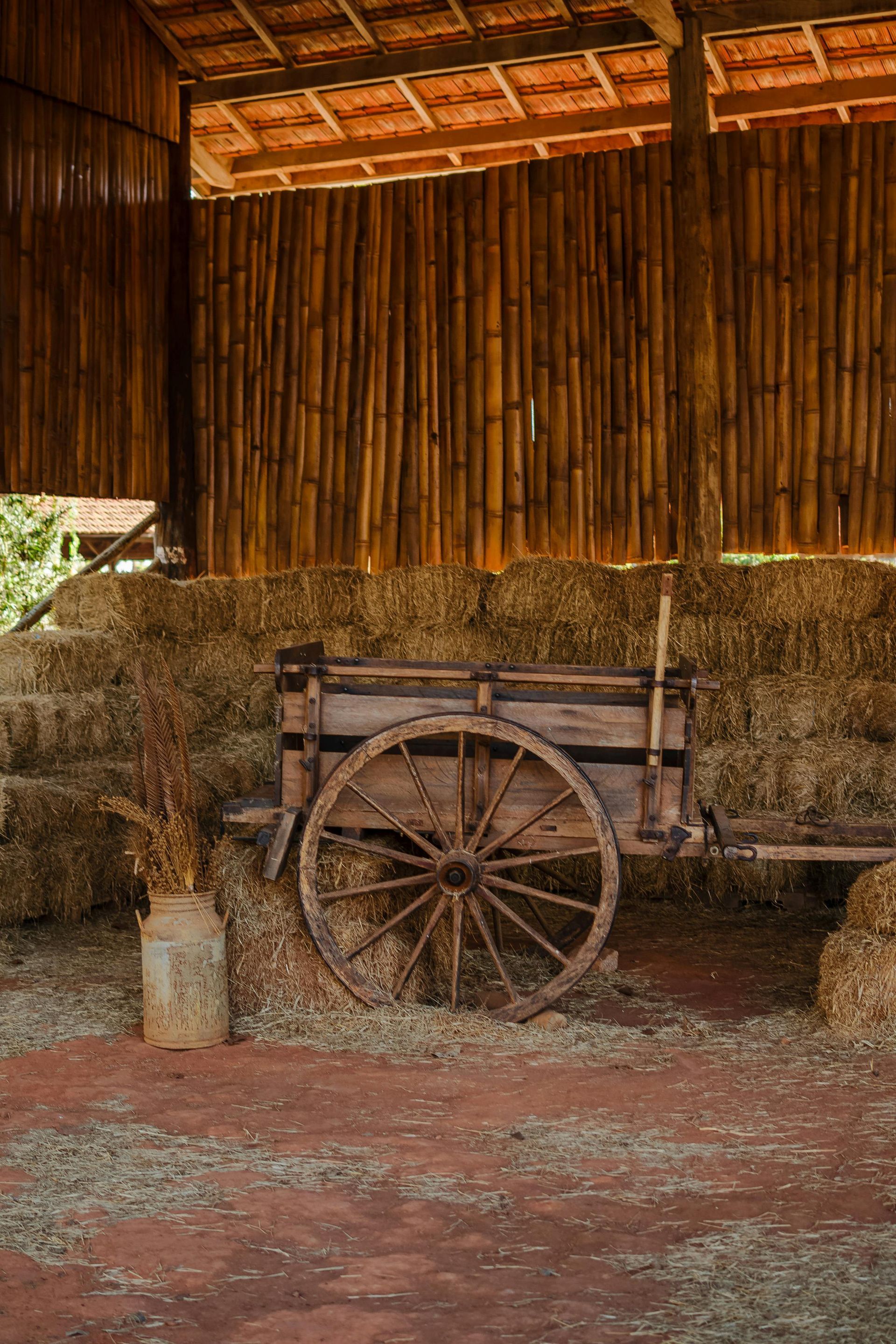Old wooden cart inside a rustic barn filled with hay bales.