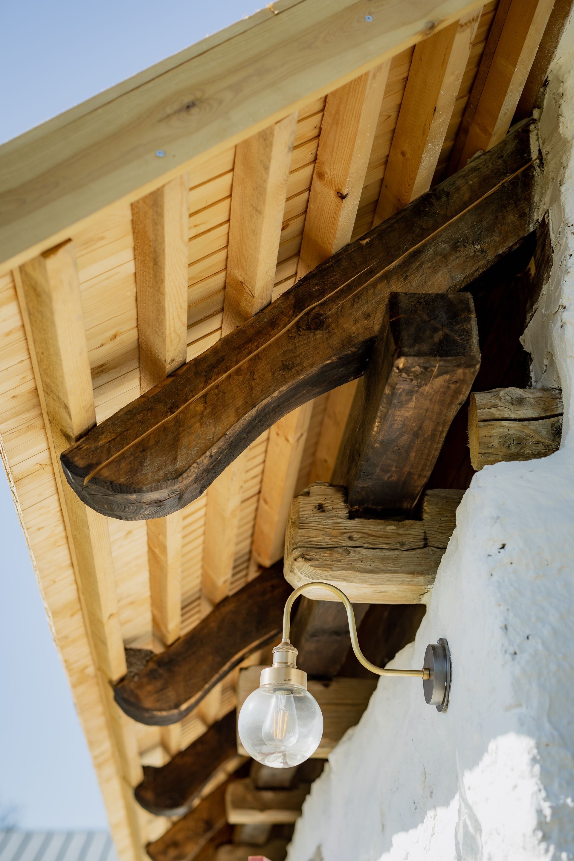 Wooden roof overhang with beams, supporting a light fixture on a white stucco wall.