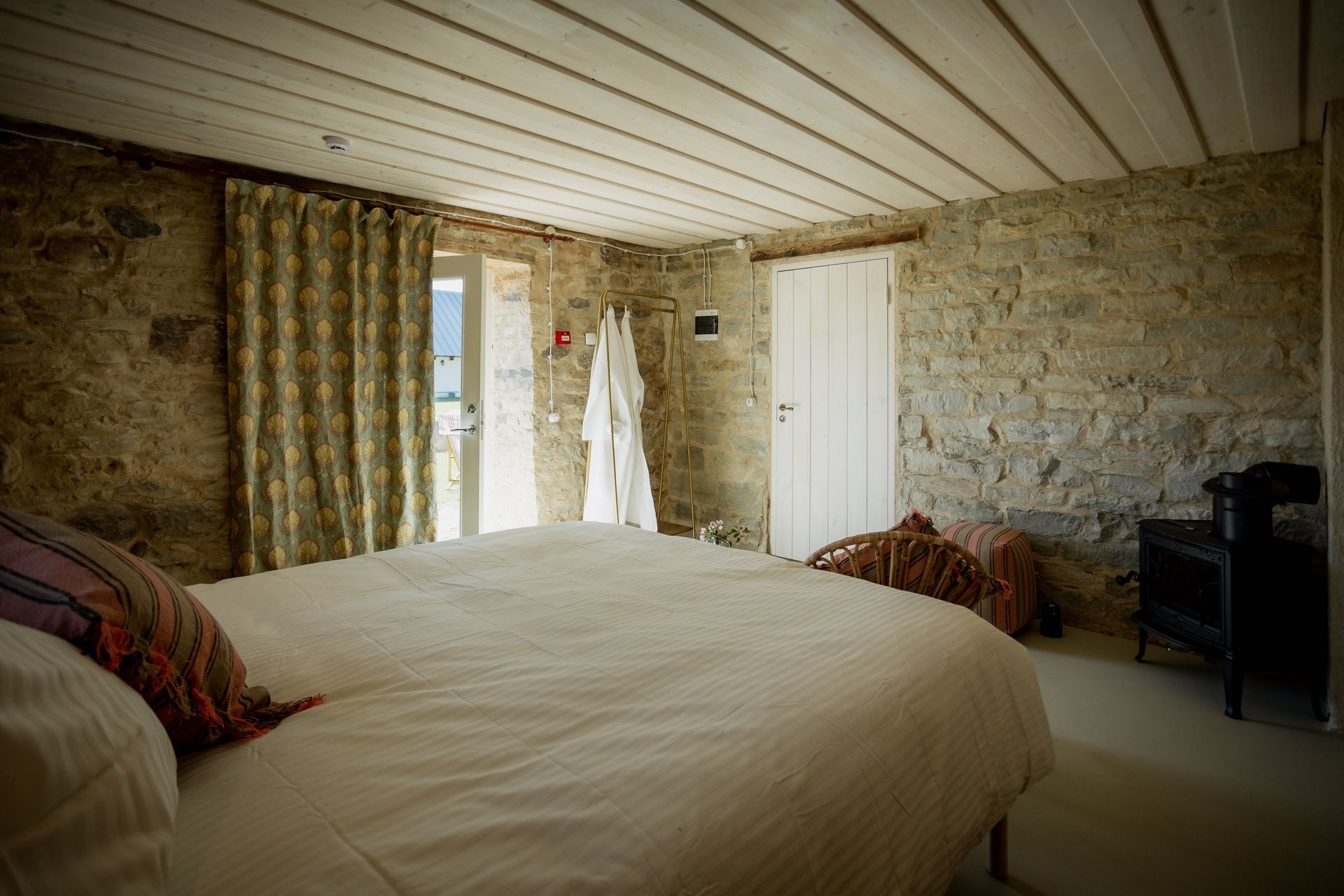 Bedroom with stone walls, white bed, open door, and white bathrobe hanging.