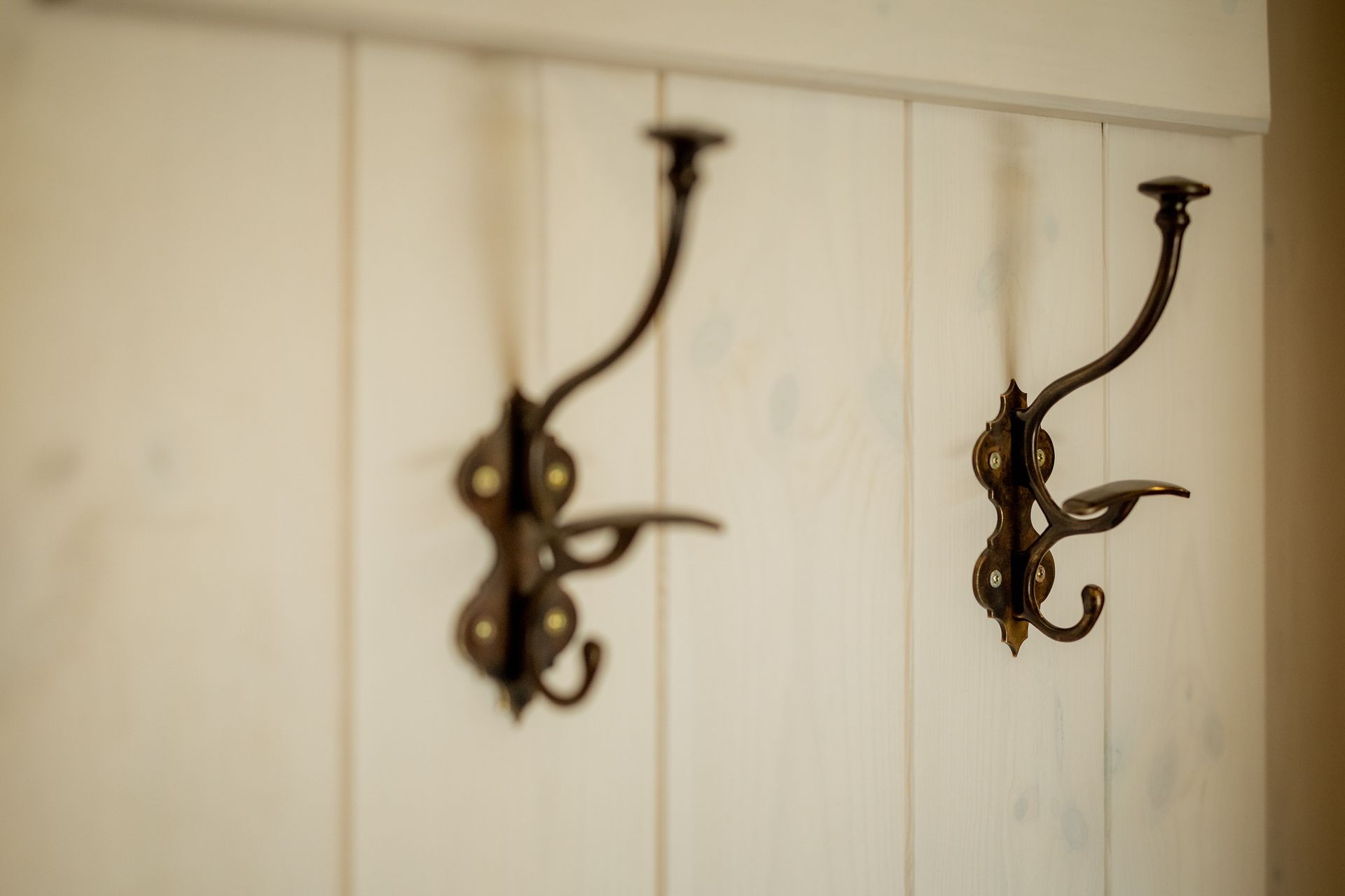 Two ornate bronze coat hooks mounted on a white wooden wall.