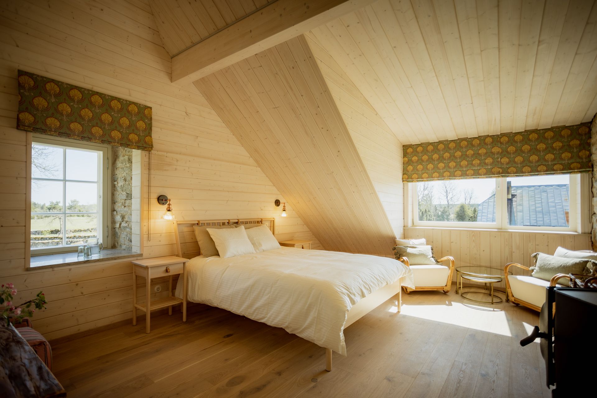 Bright wooden bedroom with a bed, chairs, and windows with patterned shades.