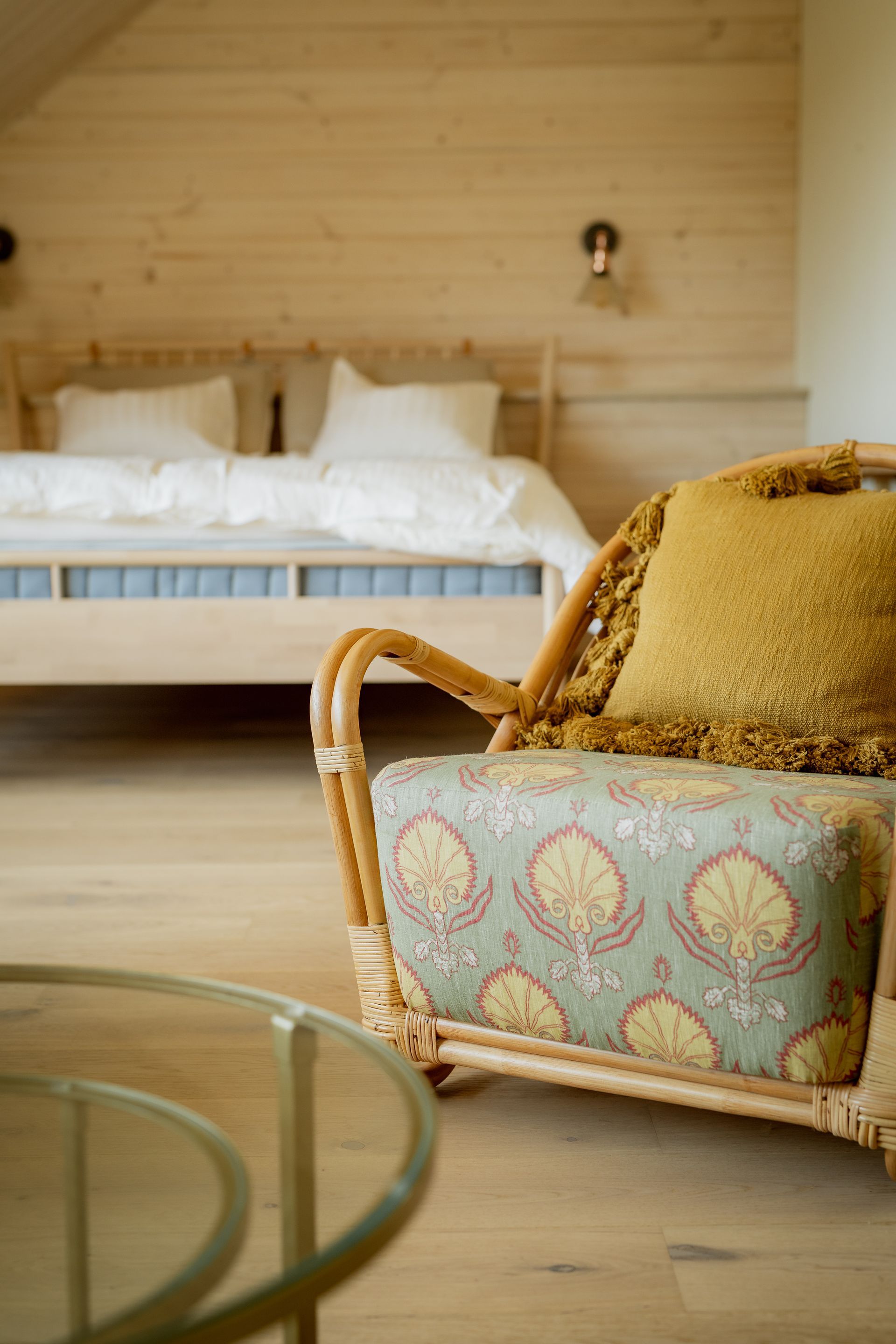 Rattan chair with floral seat cushion and yellow pillow; bedroom with bed and light wood walls.