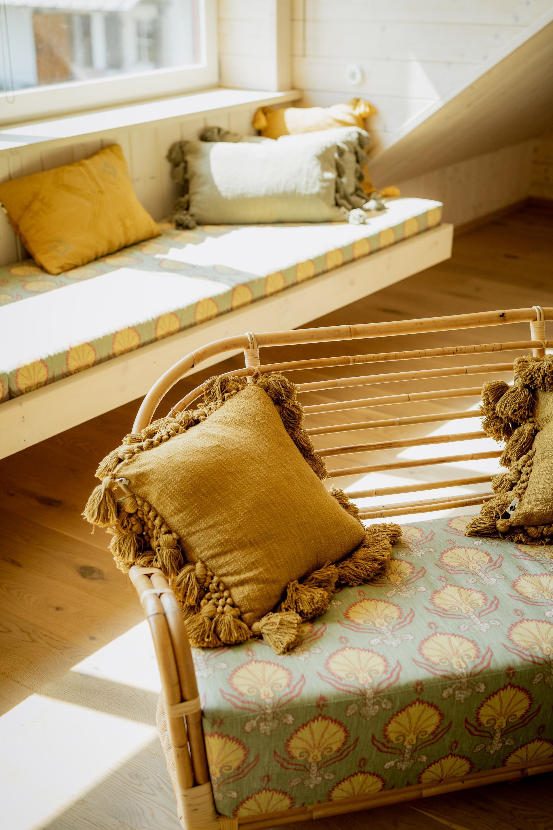 Wooden bench with patterned cushions and pillows in a sunny room with a built-in seating area.