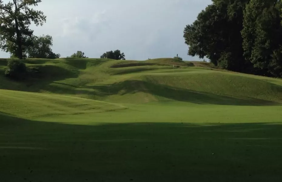 A green golf course with rolling hills under a partly cloudy sky.