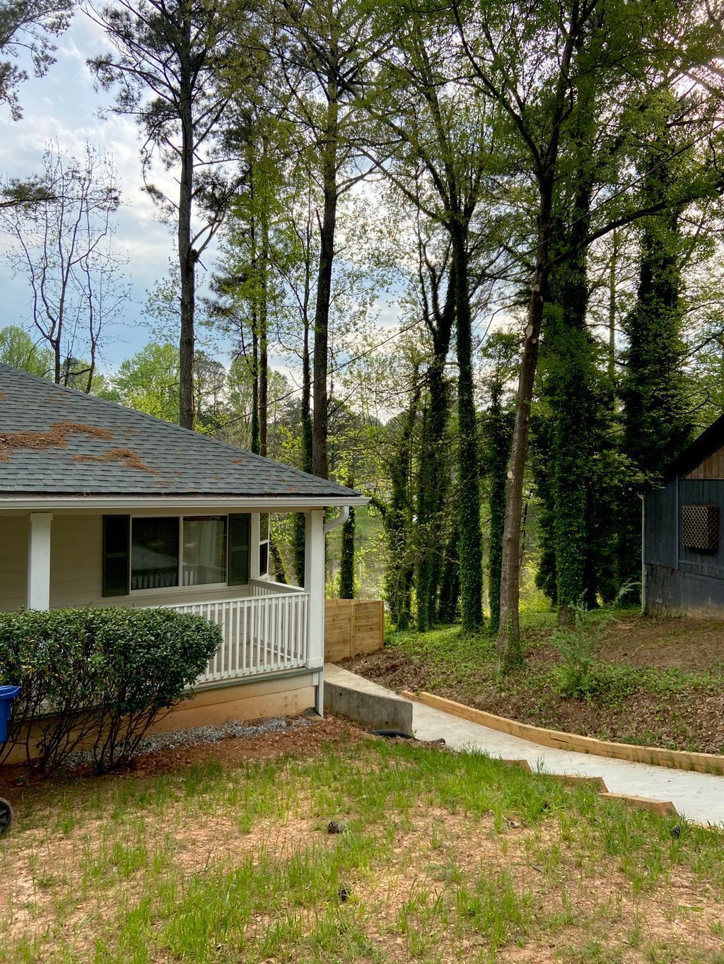 A small house with a porch and a concrete pathway leading into a wooded area.