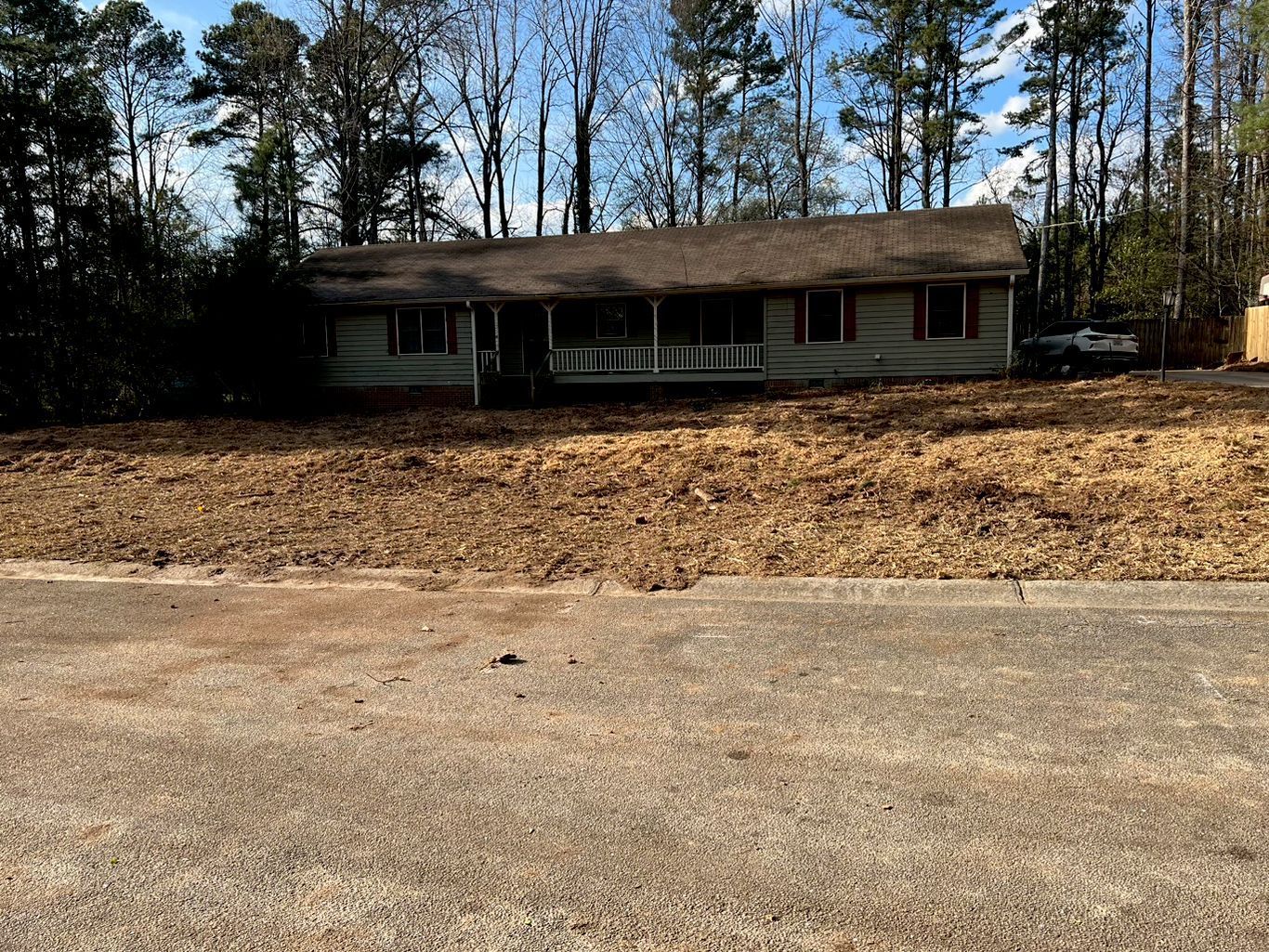 A single-story house with a porch is surrounded by trees and a yard covered in leaves.