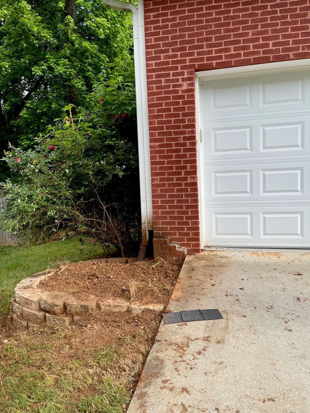 Garage next to a brick wall and a garden bed with mulch. A white garage door is open.