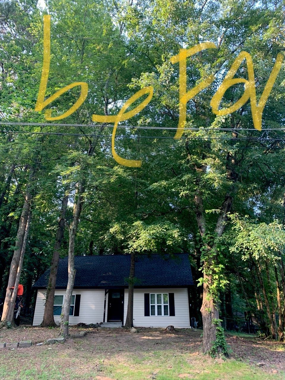 Small white house with black roof, surrounded by trees. Yellow handwritten text 