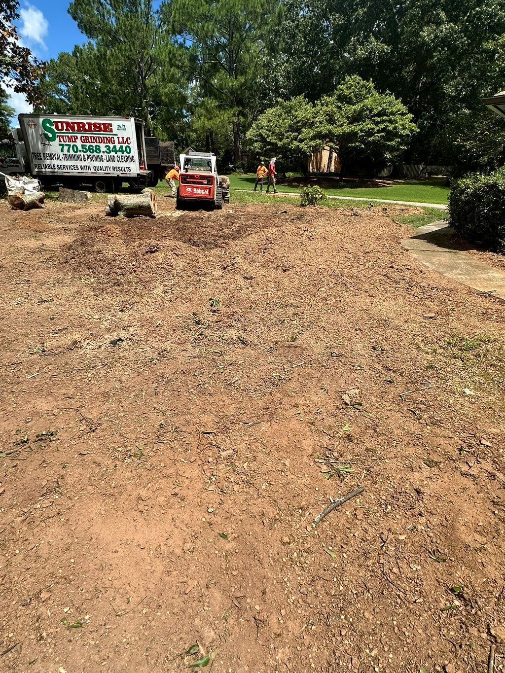 Dirt-covered area with construction equipment and workers near a moving truck, preparing a landscaping project.