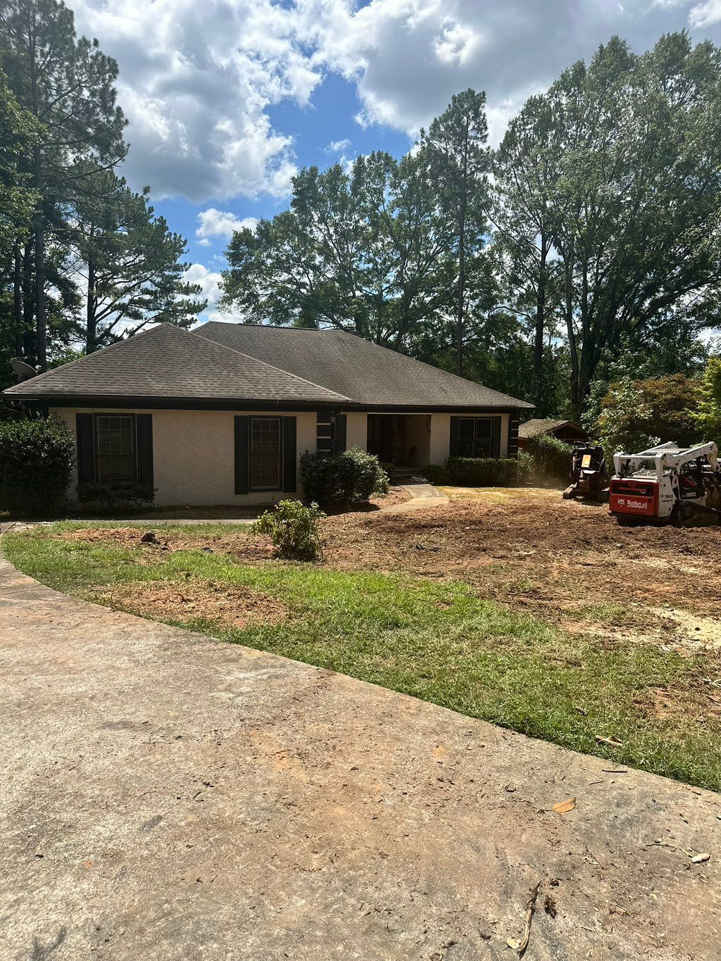 Beige house with a dirt yard, trees in the background, and construction equipment on the right.