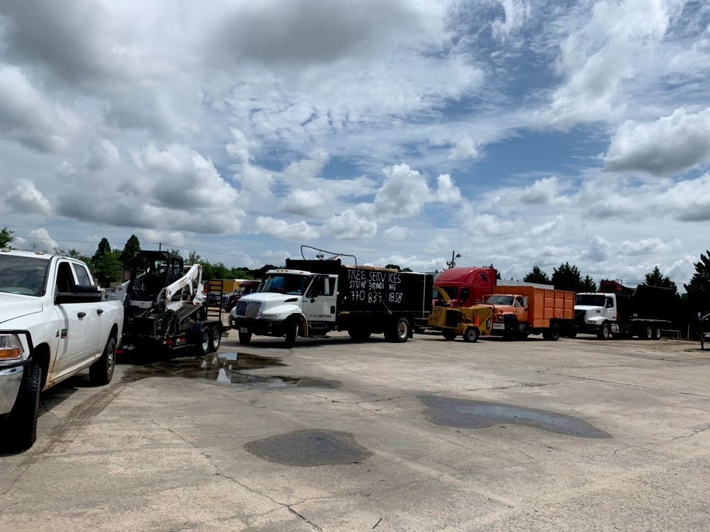 A fleet of landscaping trucks and equipment parked on a concrete lot under a cloudy sky.